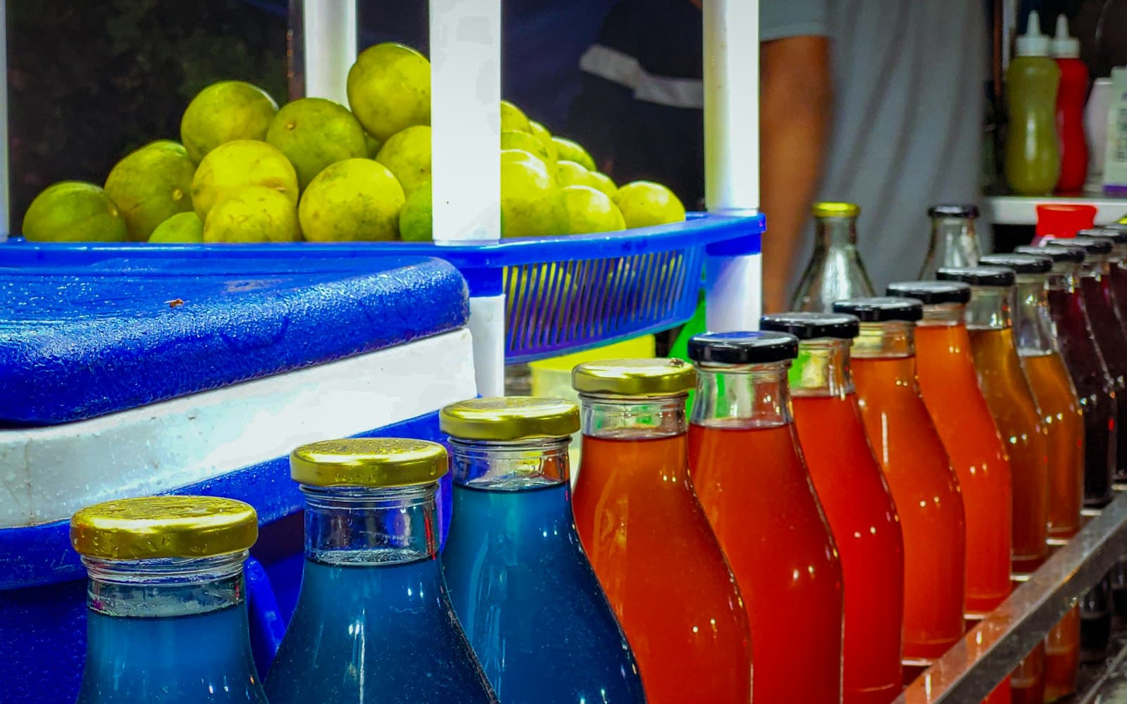 Bottled fruit juices in red, orange and blue next to fresh limes