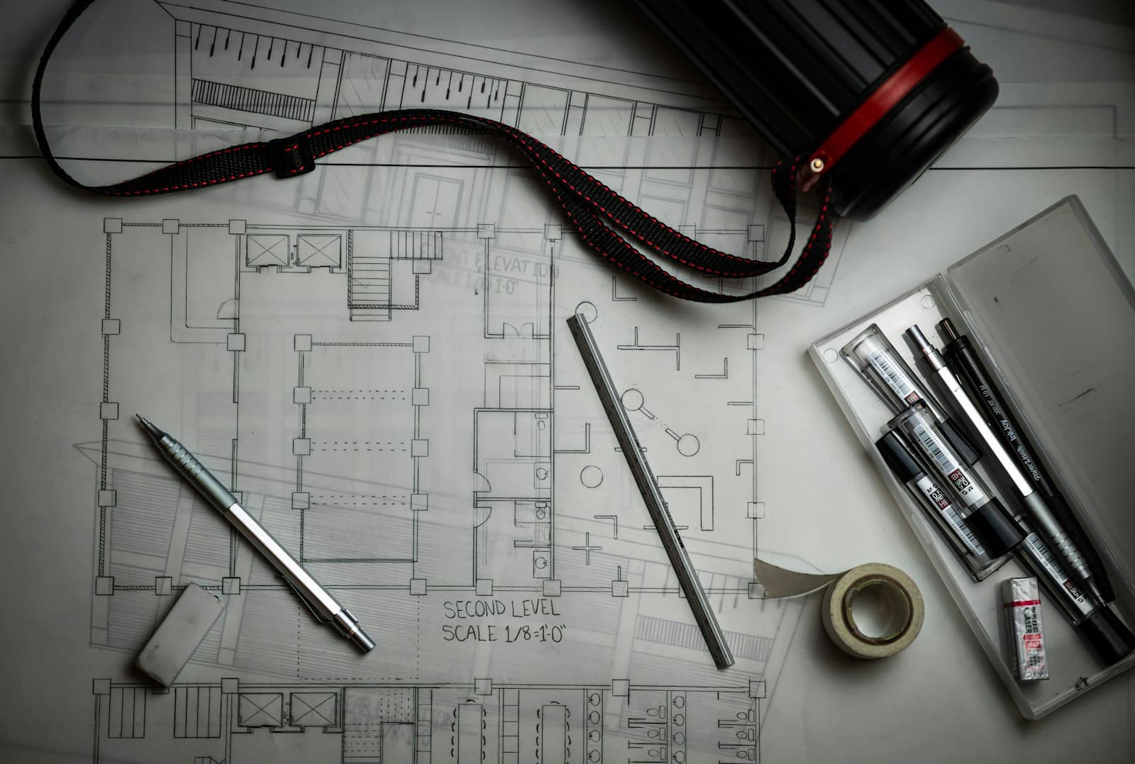 Drafting table with a floor plan, ruler and pens used for project planning