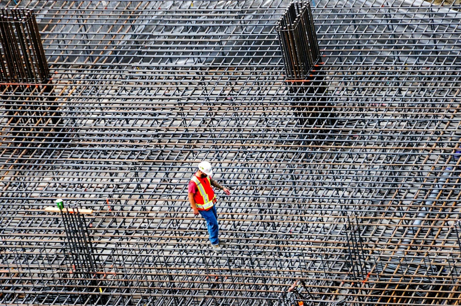 Site engineer in an orange vest walking across a large reinforcement steel mesh before a concrete pour