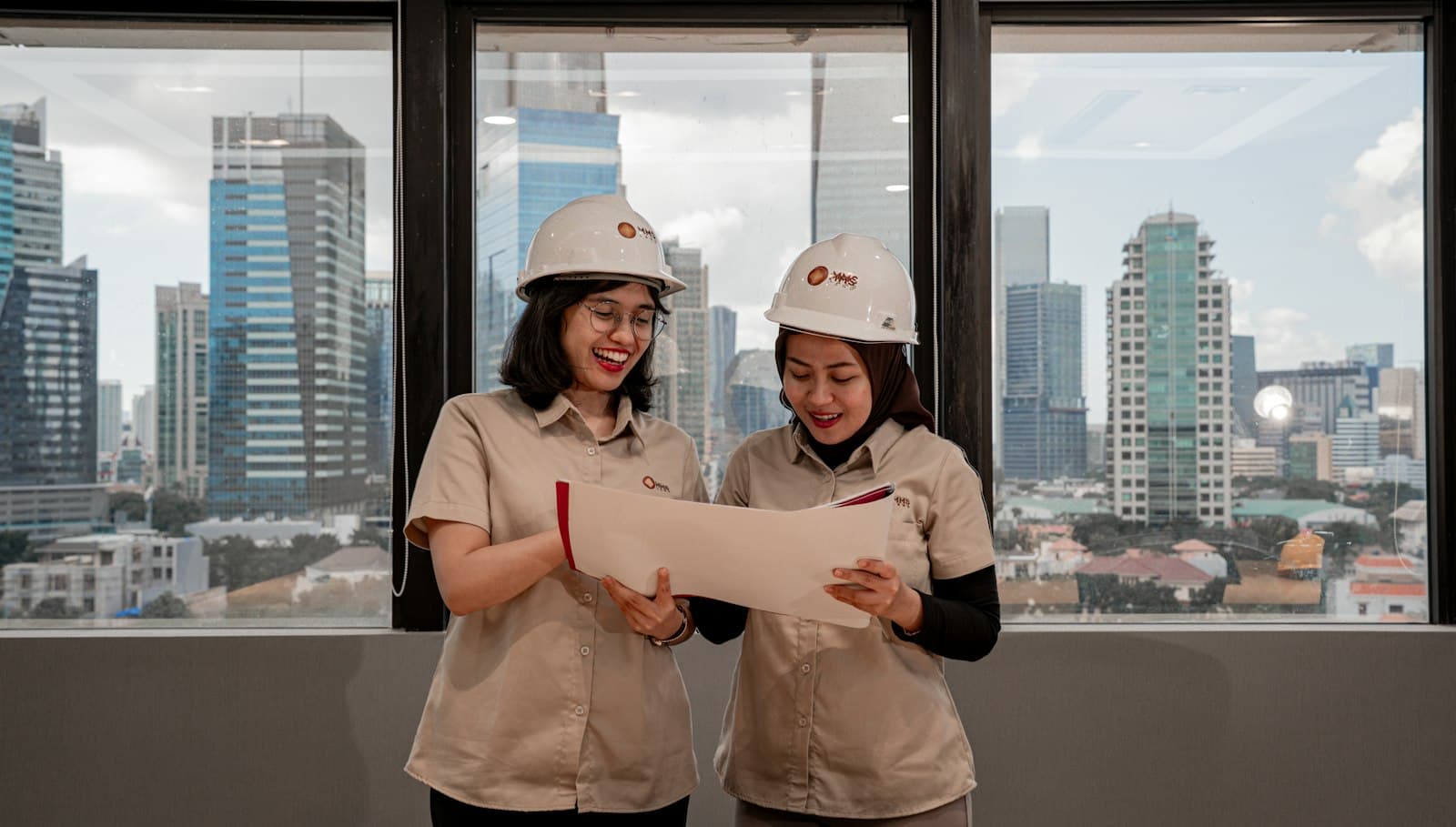 Two engineers in hard hats reviewing a drawing with a city skyline behind them