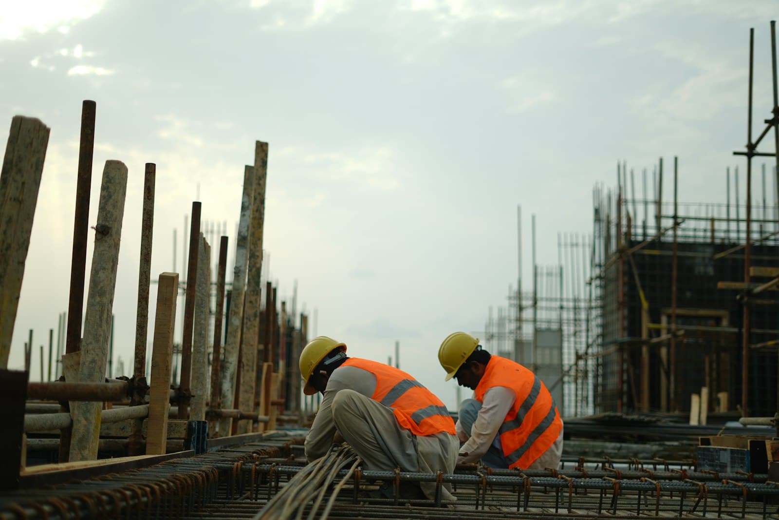 Workers in hard hats and orange vests tying reinforcement on an elevated slab