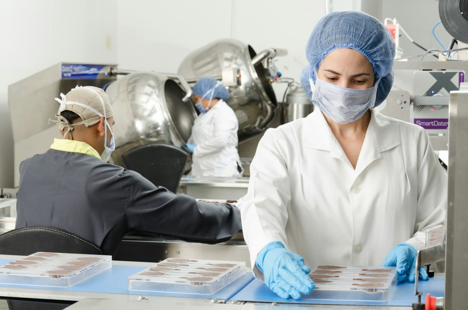 Food plant workers in hairnets and masks filling trays at a prep table